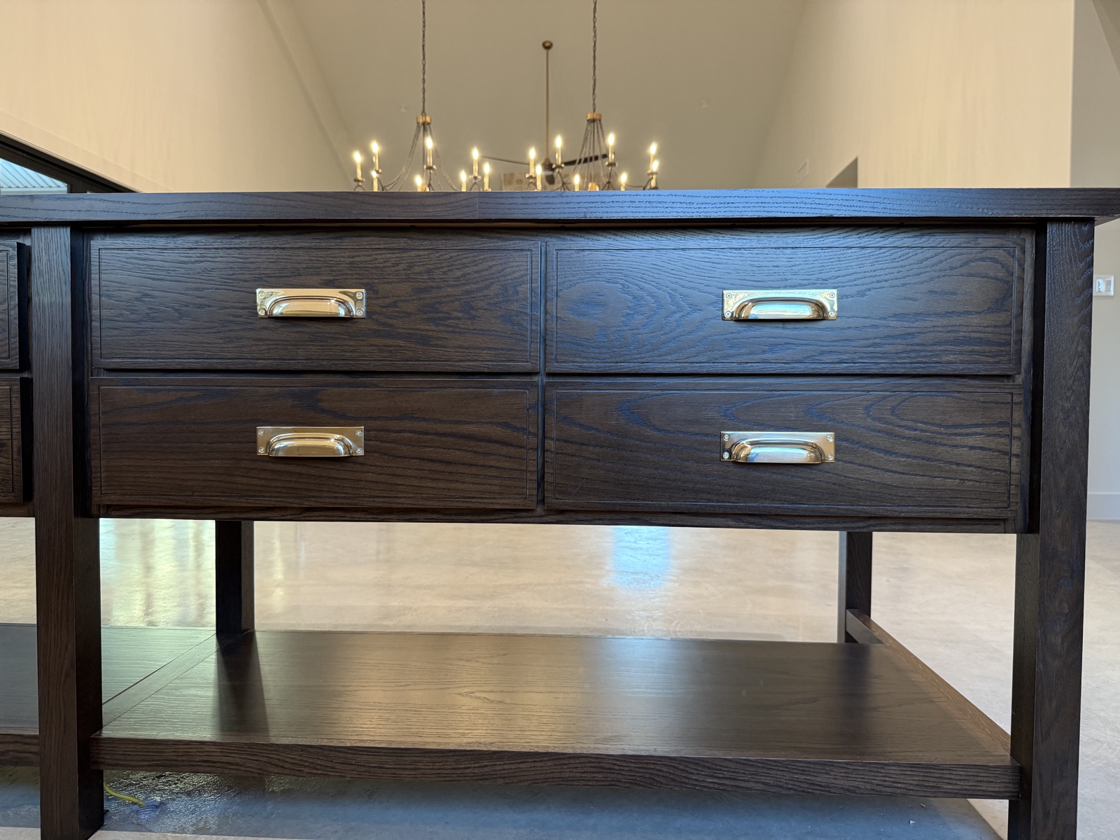 Front of the dark-stained oak island with four drawers, polished brass cup pulls, and an open shelf below