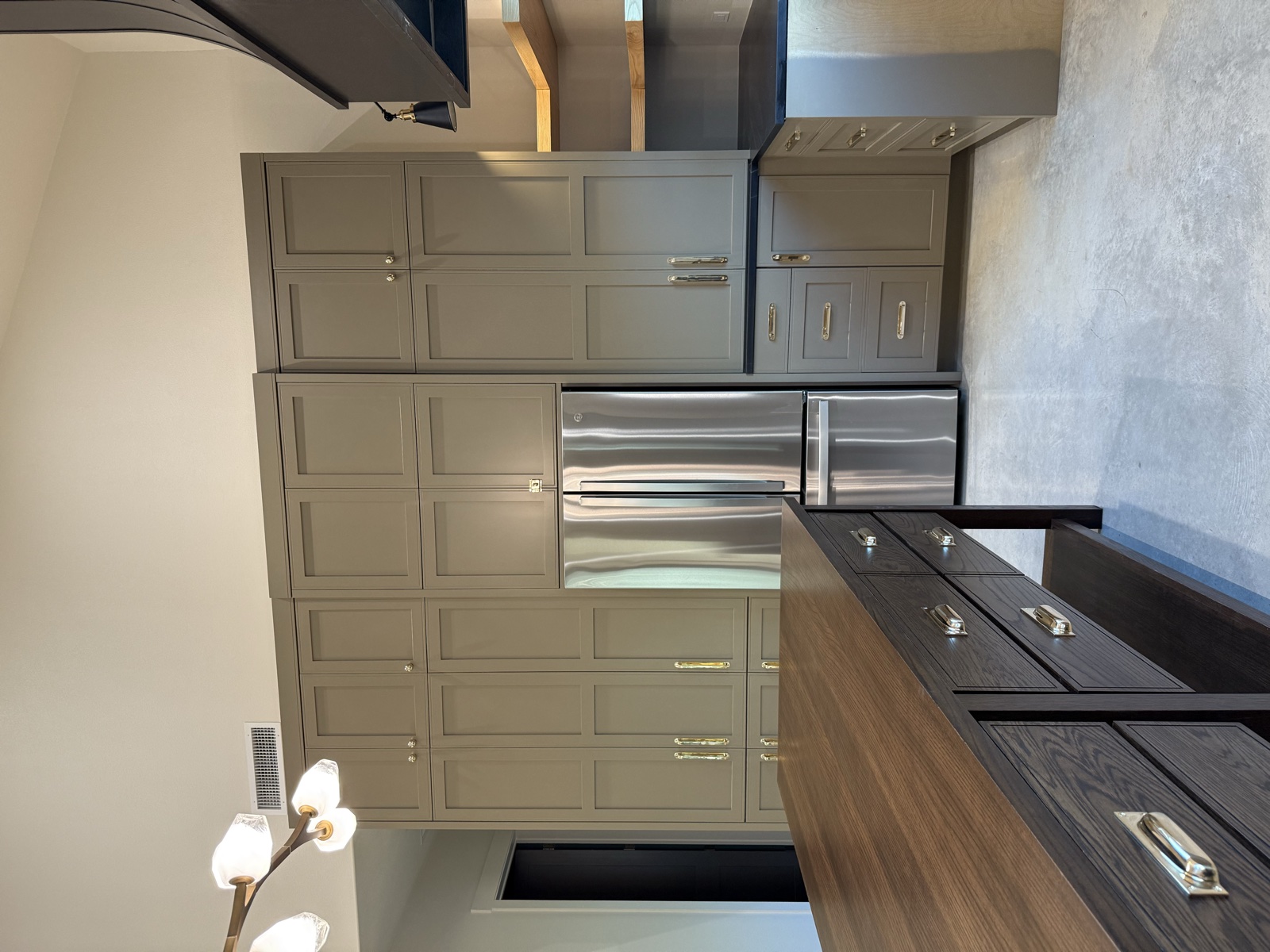 Floor-to-ceiling greige shaker cabinets built around a stainless refrigerator, beside the dark oak island