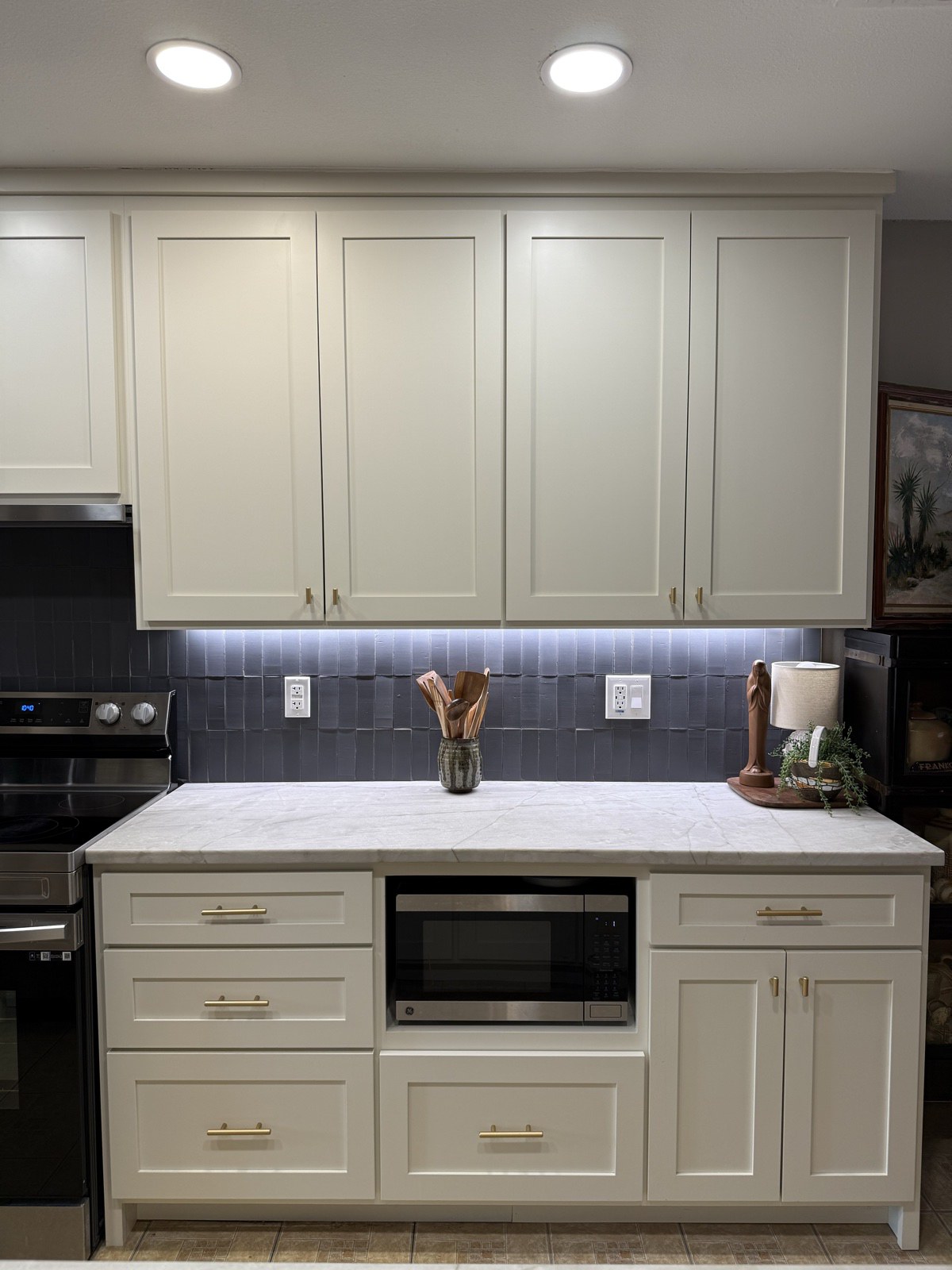 White shaker kitchen cabinets with brass pulls, a built-in microwave niche, under-cabinet lighting, and a slate blue tile backsplash