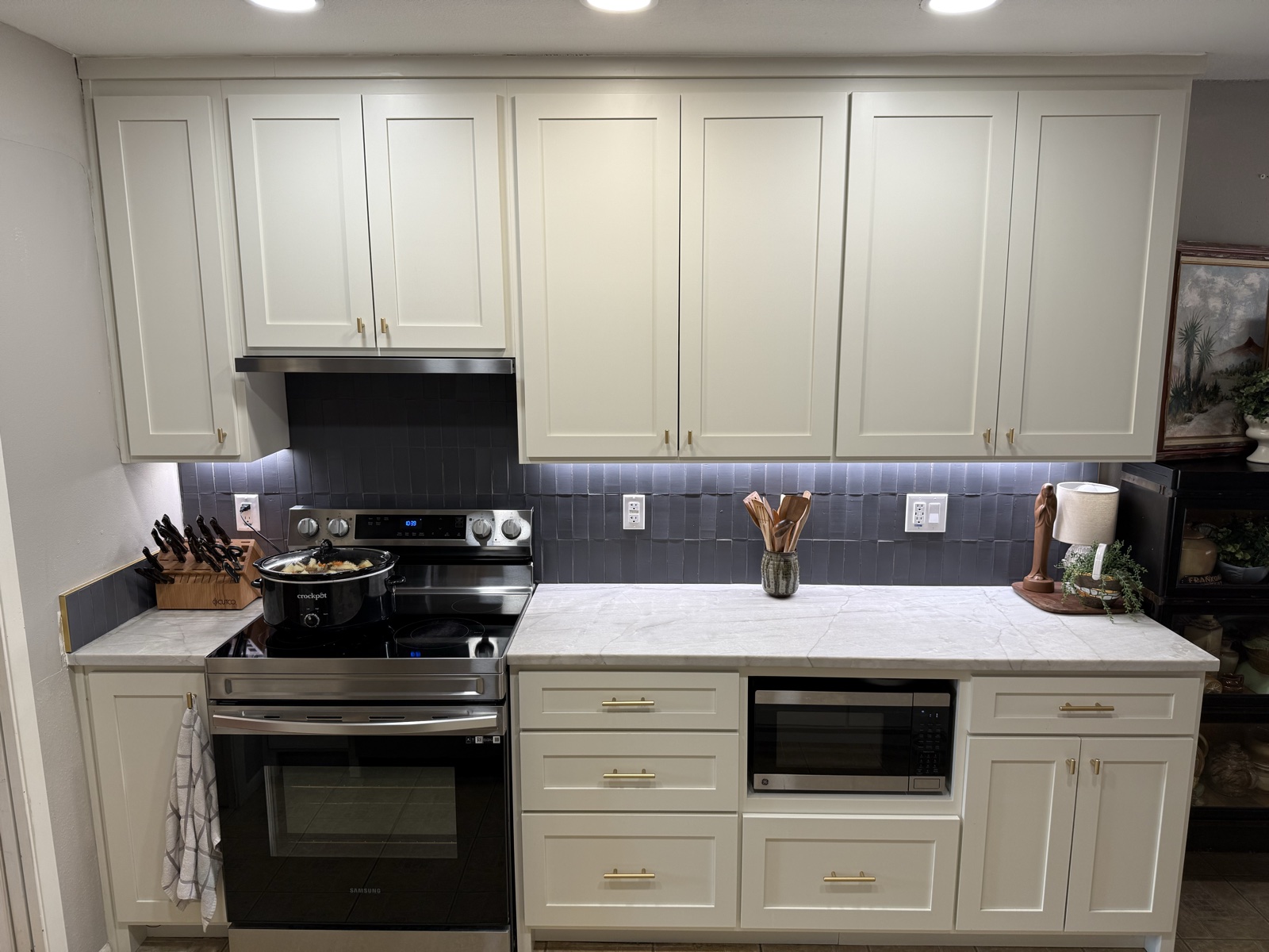 Full wall of white shaker kitchen cabinets around the range, with brass pulls, a built-in microwave, and a slate blue tile backsplash