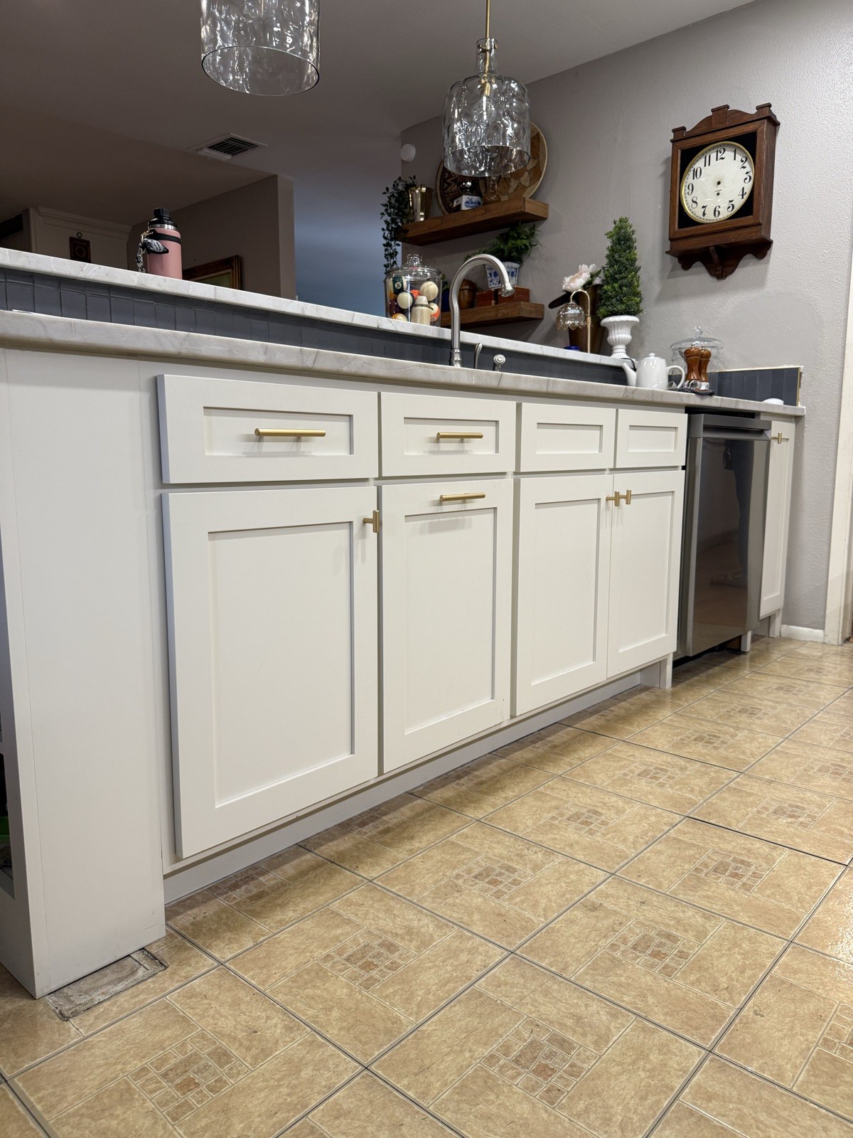 White shaker sink base cabinets and drawers with brass pulls beside a stainless dishwasher