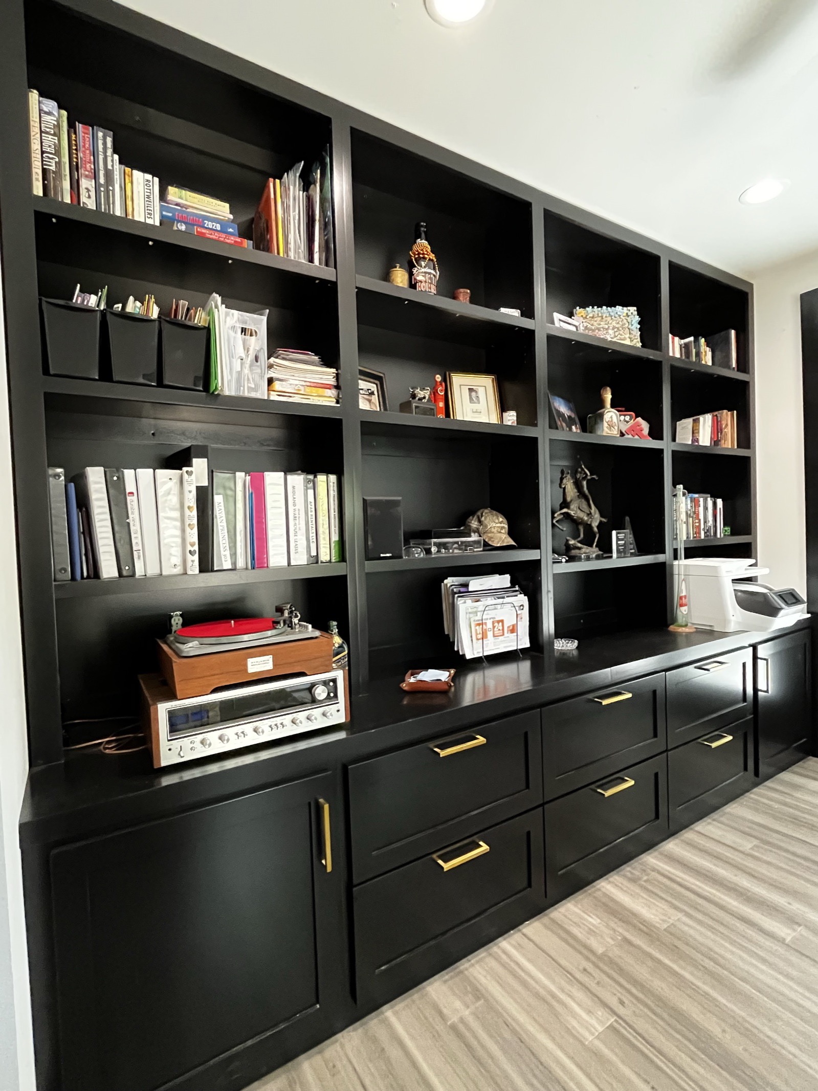 Wall of black built-in bookshelves over lower drawers and cabinets with brass pulls