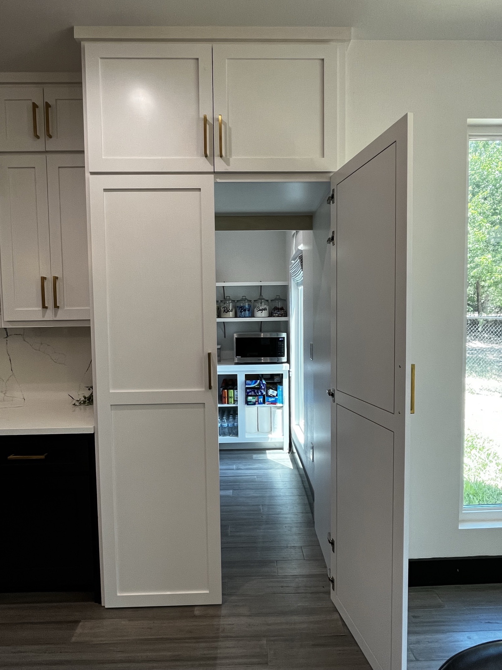 Tall white pantry cabinet door swung open to reveal a walk-in pantry hidden behind it