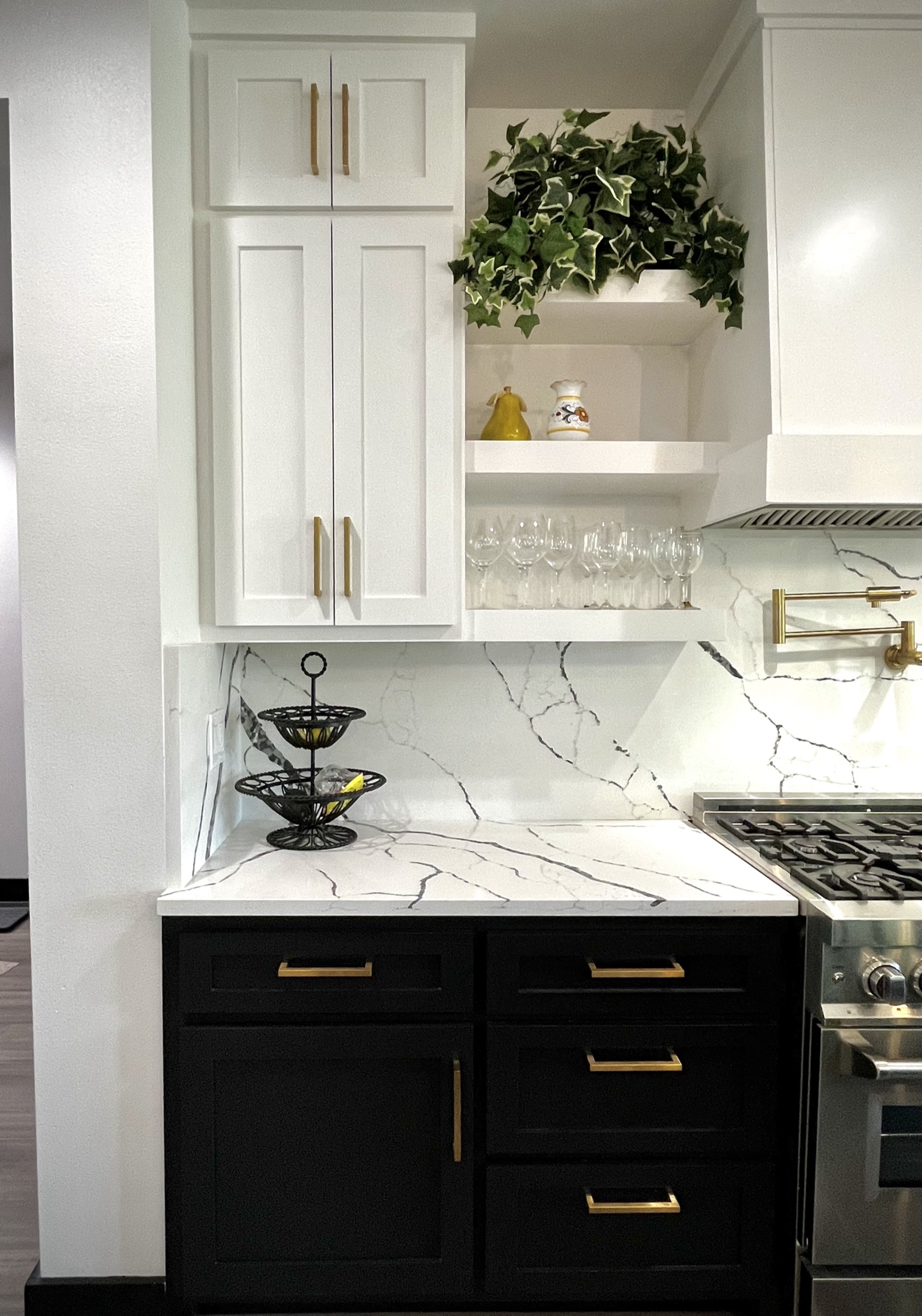 White shaker upper cabinets and open shelves above black lower drawers with brass pulls