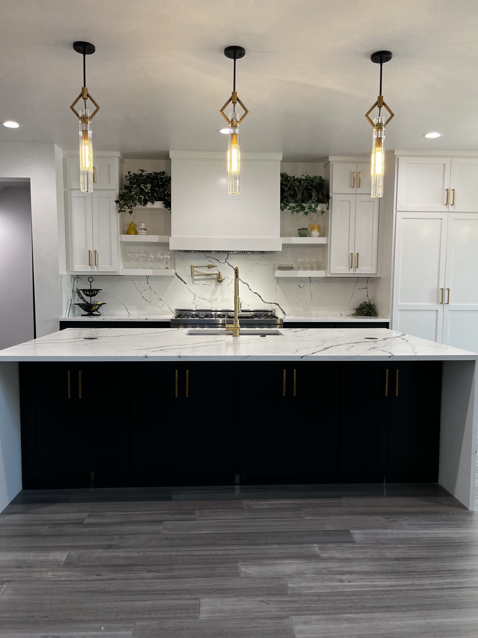 Black waterfall kitchen island with a white marble-look top under three brass and glass pendant lights